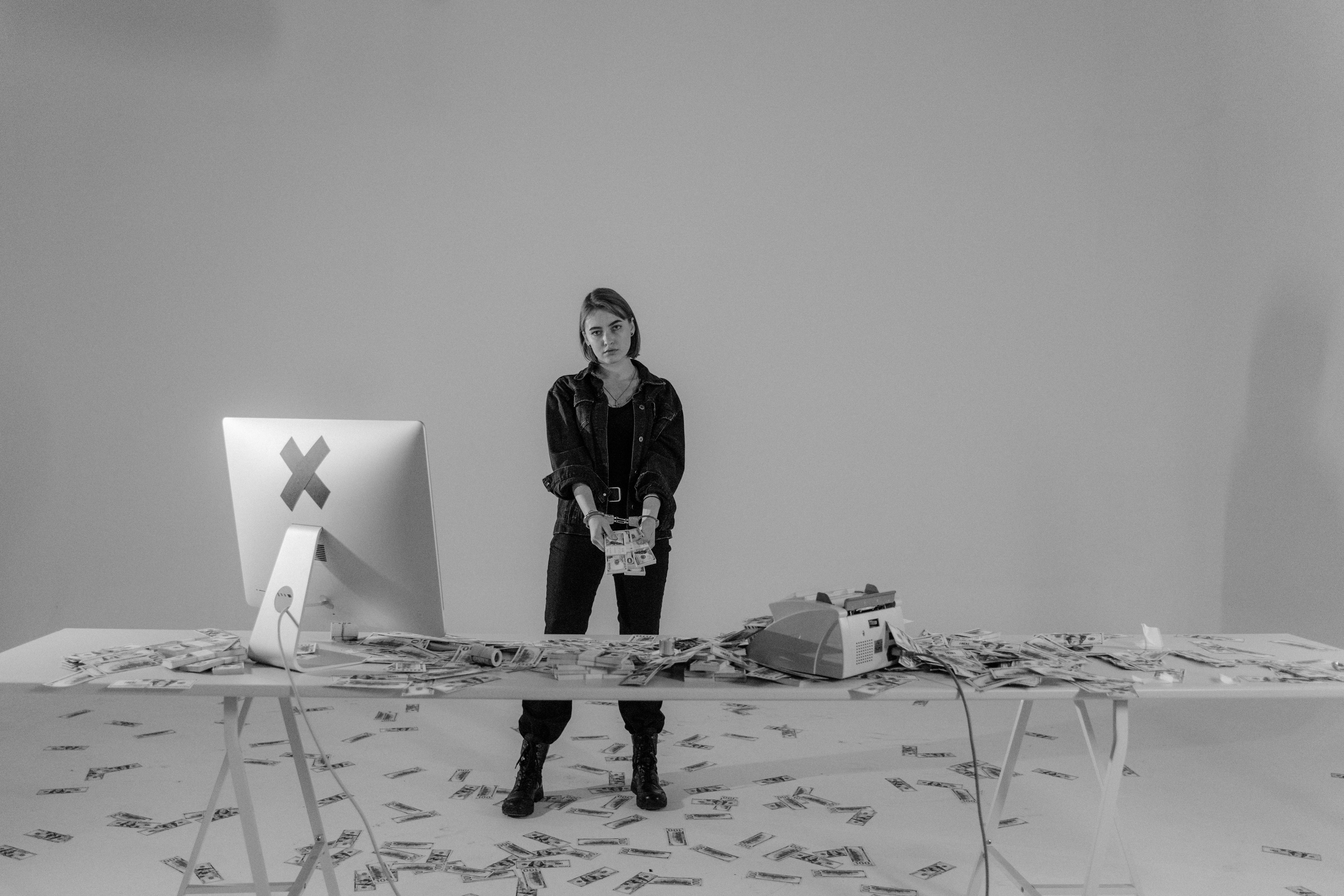 A woman stands by a table covered with money, in a monochrome minimal setup.