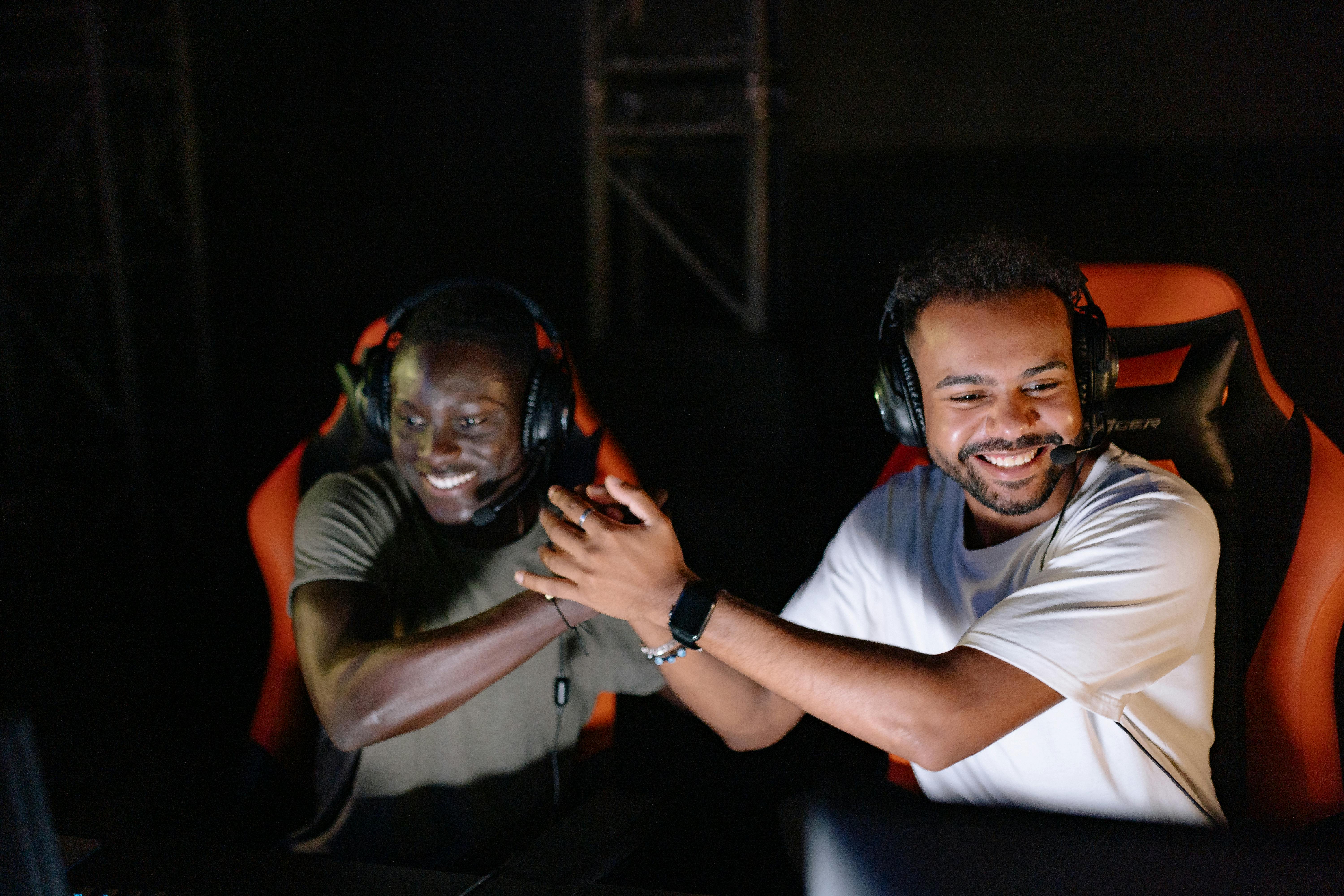 Two young male gamers celebrating a victory with a handshake and smiles in a dark gaming room.